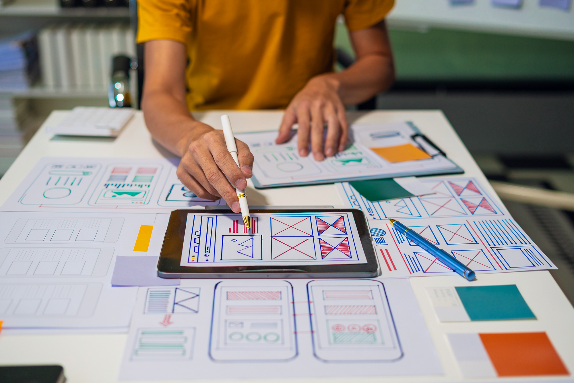 Photo of someone working on website wireframes at a desk with scattered paper and ipad